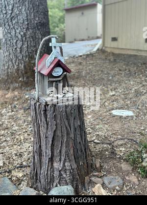 Una piccola chiesa in legno fatta a mano con tetto rosso e croce bianca montata su un ceppo d'albero in un ambiente naturale all'aperto Foto Stock