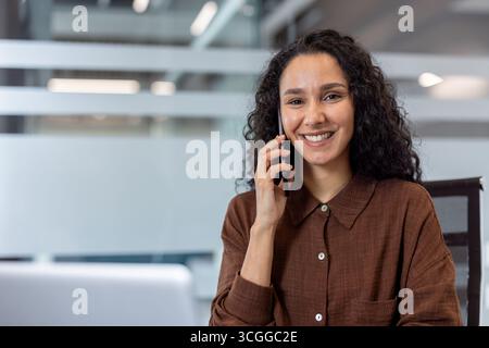 Donna felice che parla durante una telefonata in ufficio, esprimendo fiducia e disponibilità. Foto Stock