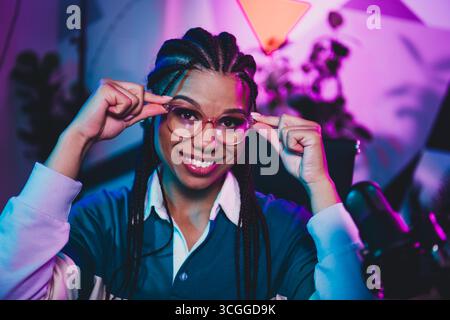 Host radio in uno spazio di lavoro illuminato che regola gli occhiali, con un aspetto professionale ed elegante Foto Stock