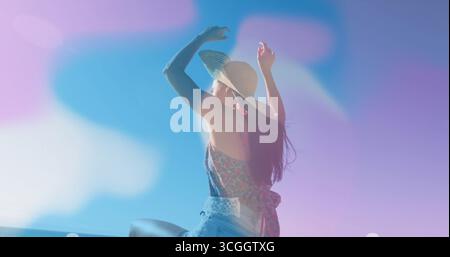 Adagiato sulla ringhiera del balcone sulla costa, donna con top floreale, pantaloncini in denim con cappello da sole in paglia regolabile Foto Stock