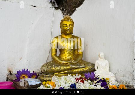 Due piccole statue di Buddha sedute con fiori freschi. Foto Stock