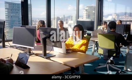 Donna africana che lavora con un laptop in un ufficio moderno con i colleghi Foto Stock