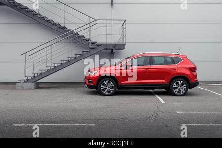 Incrocio con SEDILE rosso Ateca vicino alla scala di metallo. Vista profilo laterale del SUV compatto vicino alla parete grigia del magazzino con scala di emergenza. Foto Stock