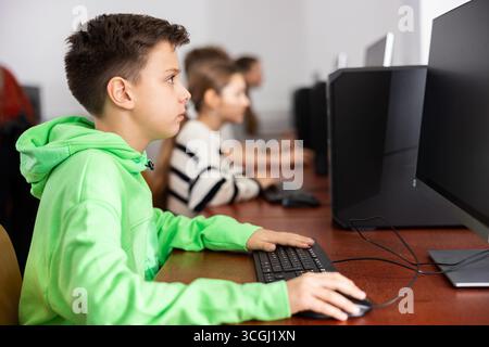 Ha messo a fuoco il ragazzo di Tween che studia con i compagni di classe in laboratorio del calcolatore Foto Stock