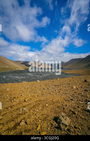 Una vallata islandese grezza dove le pendici vulcaniche dorate si incontrano con un fiume glaciale sotto cieli drammatici, incontaminata natura selvaggia nordica Foto Stock