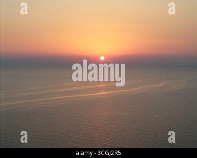 Il sole tramonta sul mare Egeo a Kassandra, in Grecia, dipingendo il cielo con colori caldi in una scena tranquilla e bella, perfetta per viaggi e tour Foto Stock