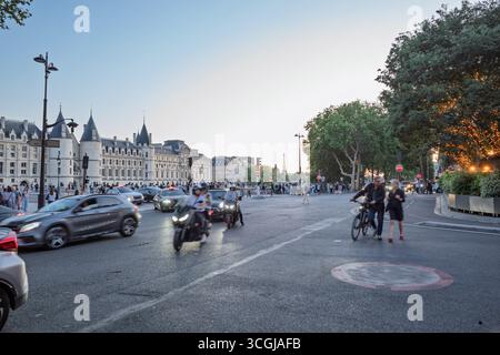 Un'affollata scena di strada parigina al tramonto con auto, moto, pedoni e la Torre Eiffel leggermente visibile sullo sfondo. Foto Stock