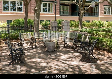 Charleston, South Carolina, Stati Uniti - 2 luglio 2025: Cerchio di panche in ferro battuto sotto alberi ombrosi in un parco di Charleston con sentieri in mattoni e vegetazione. Foto Stock