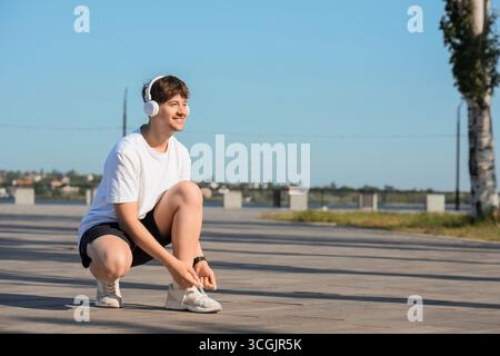 Runner maschile con cuffie che legano lacci di scarpe sul terrapieno Foto Stock