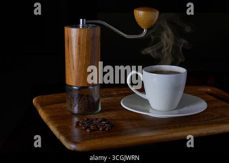 Una scena ancora più naturale del processo di preparazione del caffè, dai chicchi tostati al macinacaffè manuale con caffè macinato e una tazza calda. Un concetto per il caffè artigianale, Foto Stock