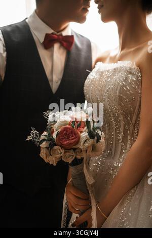 Primo piano di sposi e sposi con abito da sposa con perline e bouquet floreale Foto Stock