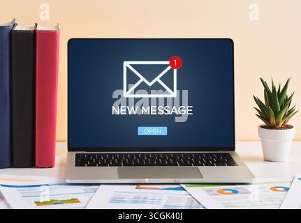 Laptop che visualizza sullo schermo un nuovo messaggio di notifica, posizionato su una scrivania con documenti e libri in un ufficio Foto Stock