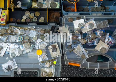 Ipoh, Malaysia - 17 agosto 2025: Una vista dall'alto di varie vecchie monete, alcune confezionate in plastica, esposte in casse di plastica aperte presso un venditore ambulante" Foto Stock