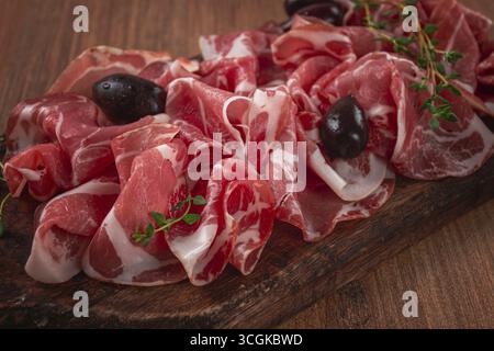 Carne secca appena tagliata, servita con olive ed erbe aromatiche, su un tagliere di legno, nessuno Foto Stock