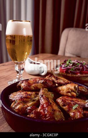 Deliziose ali di pollo alla griglia, con patatine fritte, insalata e una bevanda rinfrescante, a un tavolo accogliente, non ci sono persone Foto Stock