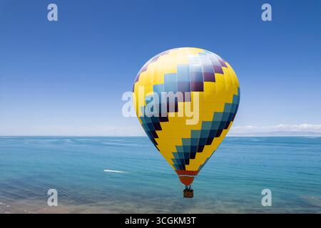 La vivace mongolfiera galleggia sul vasto lago blu del Qinghai. Questa tranquilla scena di viaggio mostra avventure panoramiche e vedute del cielo limpido. Foto Stock