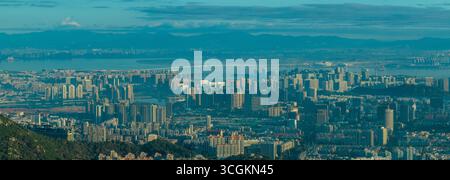 La città di Xiamen in Cina mostra un vasto paesaggio urbano caratterizzato da molti edifici moderni, una baia tranquilla e catene montuose lontane. Foto Stock