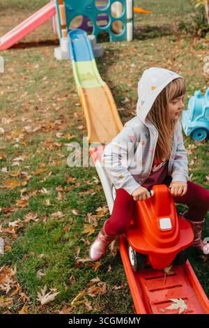 Ragazza in età prescolare che cavalca un'auto giocattolo su uno scivolo in autunno Foto Stock