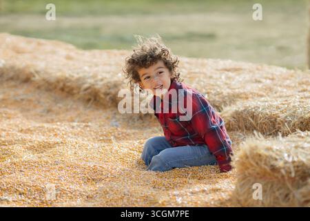 Bambino sorridente in camicia a quadri seduto nella fossa di mais presso la toppa di zucca dello Utah Foto Stock