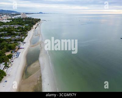 Vista aerea della tranquilla spiaggia che incontra la vasta distesa del mare con edifici e vegetazione lussureggiante visibili in lontananza, Hua Hin, Prachuap Khiri Khan, Thailandia. Foto Stock