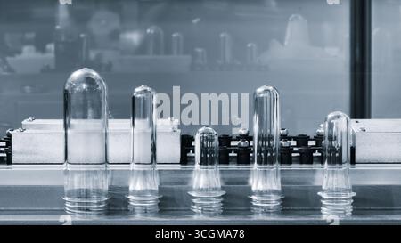 Preforme in plastica PETG per la produzione di bottiglie sul nastro trasportatore prima della pressa per soffiaggio a caldo Foto Stock