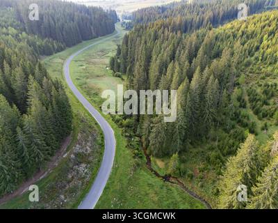 Veduta aerea di una strada tortuosa che attraversa la verdeggiante valle dolina di Kamenista a Veporske Vrchy, fiancheggiata da fitte foreste, Sihla, regione di Banská Bystrica, Slovacchia. Foto Stock