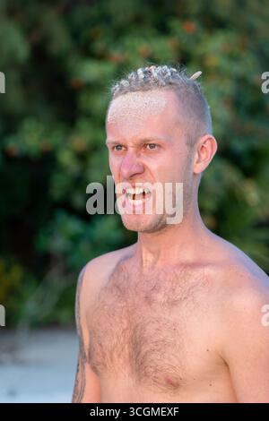 Ritratto di un giovane aggressivo con dreadlocks sulla testa in natura sulla spiaggia tropicale, da vicino Foto Stock
