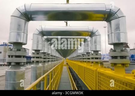 Forma ad arco dei tubi sopra la piattaforma di ispezione. Condotte e valvole a saracinesca in un impianto di produzione e stoccaggio di gas naturale liquefatto. Foto Stock