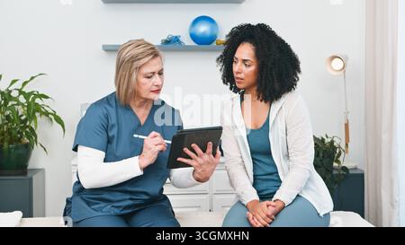 Un fisioterapista esperto si impegna con un giovane cliente nero, esaminando il piano di trattamento personalizzato su un tablet digitale Foto Stock
