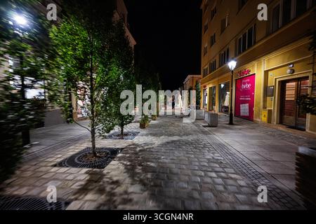 Rzeszow, Polonia - 22 agosto 2025: Una strada vivace a Rzeszow, Polonia di notte con negozi illuminati e vegetazione Foto Stock