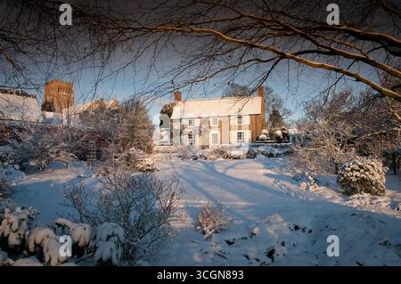 Un'affascinante casa si trova in mezzo a un giardino innevato, con rami che mostrano gelo e luce soffusa che creano un'atmosfera invernale serena. Foto Stock