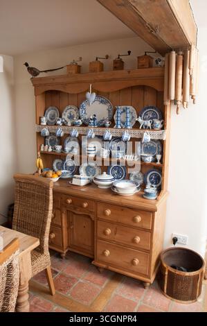L'armadietto in legno splendidamente arredato mostra una gamma di piatti in ceramica blu e bianca in una calda atmosfera da cucina. Foto Stock