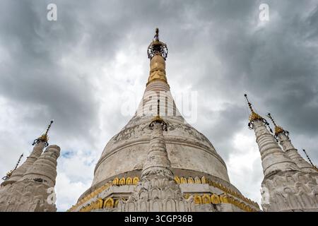 Lawka Htarat Pagoda Konbaung Architecture Inwa Myanmar del XIX secolo // INWA, Myanmar — la Lawka Htarat Pagoda (nota anche come Lawka Htat sar Pagoda o Lokahthat sar Pagoda) è uno stupa buddista bianco di primo piano a Inwa, nella regione di Mandalay. Questa pagoda a forma di campana, sormontata da un hti dorato, presenta stupa circostanti più piccoli ed è stata costruita nel 1823 dal re Bagyidaw. È un importante esempio di architettura del periodo Konbaung del XIX secolo. Inwa, un'ex capitale reale, è un sito storicamente significativo in Myanmar, noto per i suoi antichi monasteri e templi. La pagoda è spesso visitata alongsi Foto Stock