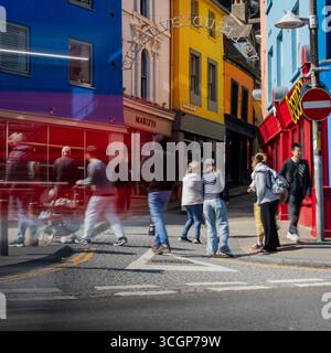 La vivace scena di strada con edifici colorati e pedoni in movimento si confondono lungo una trafficata strada dello shopping nel centro della città nel Regno Unito. Foto Stock