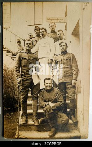 Il personale militare della cucina dell'esercito austro-ungarico durante la prima guerra mondiale soldati in uniforme, tutti con baffi, posano su una scala. Dietro di loro c'è un cartello con l'iscrizione Zahnambulatorium (clinica odontoiatrica). La fotografia è stata probabilmente scattata da qualche parte in Italia. Foto Stock