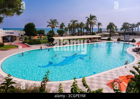 belek, Turkiye, 27.07.2025 persone che si rilassano presso una grande piscina dell'hotel con acqua blu e un mosaico di delfini sul mare. Vacanze estive. Foto Stock