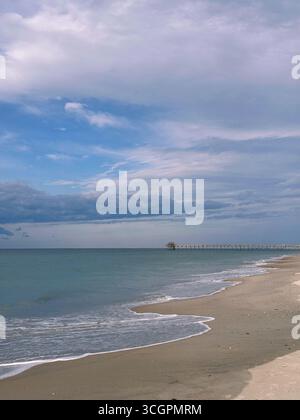 Un lungo molo di legno si estende nell'oceano sotto un cielo parzialmente nuvoloso, con onde dolci e costa sabbiosa. Molo Oceanana, Atlantic Bea Foto Stock