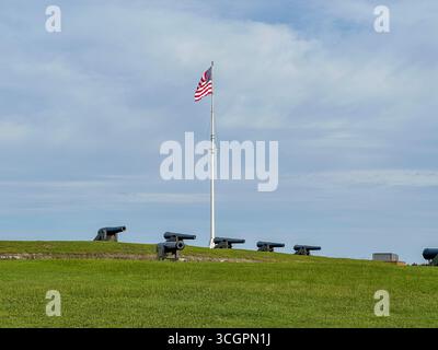 Fila di cannoni storici posizionati lungo i bastioni erbosi del Fort Macon State Park nel North Carolina, con la bandiera americana che sventola orgogliosamente sopra. Foto Stock