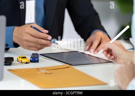 Consulenza assicurativa. Discussione della polizza assicurativa auto con il cliente che utilizza tablet e modellini di auto. Foto Stock