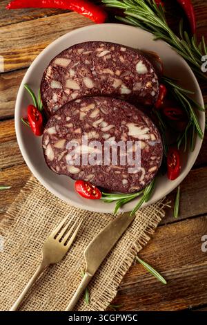 Salsiccia di sangue con frattaglie di carne accompagnate da rosmarino e pepe rosso su un tavolo di legno. Foto Stock