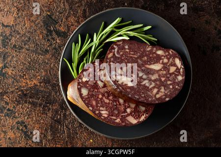 Salsiccia di sangue con frattaglie di carne accompagnata da rosmarino su un piatto nero. Foto Stock