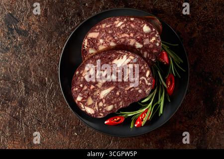 Salsiccia di sangue con frattaglie di carne accompagnata da rosmarino e pepe rosso su un piatto nero. Foto Stock