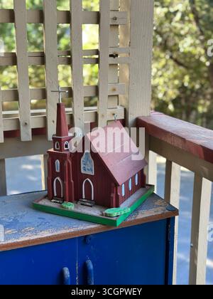 Un modello in legno artigianale di una piccola chiesa rossa con dettagli a campana e dipinti, collocato su uno scaffale all'aperto in luce naturale. Foto Stock