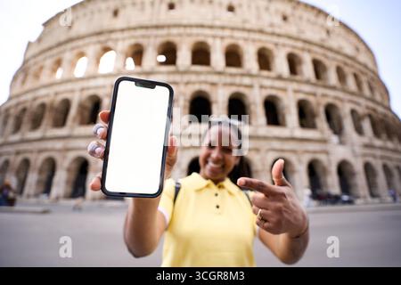 Donna turistica che mostra smartphone con schermo vuoto di fronte al Colosseo di Roma. Foto Stock