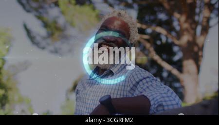 Uomo anziano sorridente appoggiato a ringhiere in legno in giardino, con camicia a scacchi e orologio da polso Foto Stock