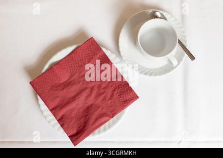 Svuotare la tazza di caffè e un piatto con un tovagliolo rosso su un tavolo. Vista dall'alto. Oggetti relativi al tè e al consumo di torte con la famiglia. Foto Stock