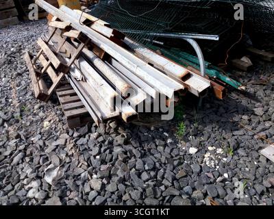 Pile di lamiere laminate e altri materiali metallici sono collocate su una superficie di ghiaia in un cantiere edile, mostrando varie trame e colori Foto Stock