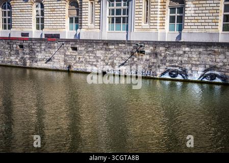 Gand, Belgio, 31.03.2025, Un edificio storico in pietra a Gand, Belgio, si affaccia sul canale con finestre ad arco sopra e graffiti sul muro, tra cui Foto Stock