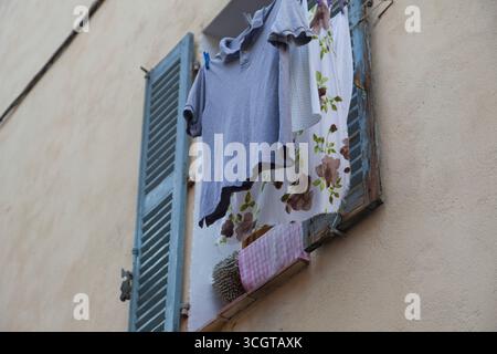Indumenti che si asciugano fuori da una finestra vicino ad alcune persiane su una parete Foto Stock
