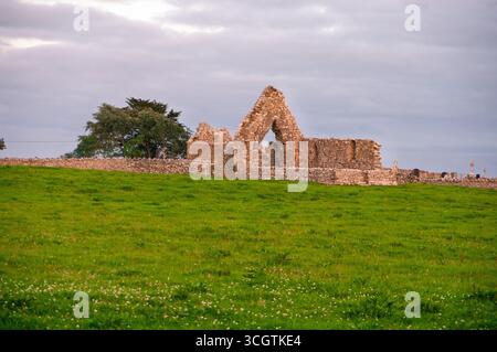 Un grande edificio in pietra si trova su di una collina con un lussureggiante campo verde davanti ad esso. Il cielo è nuvoloso e il sole sta tramontando, creando un ambiente tranquillo e rilassante Foto Stock